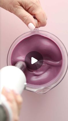 a person holding a blender filled with purple colored food and mixing it into a bowl