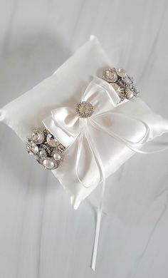 a white ring pillow with bows and pearls on it's side, sitting on a table