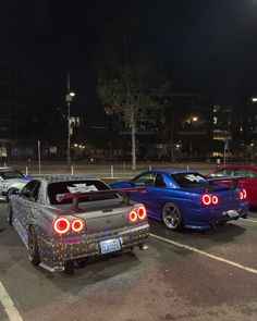 three cars are parked in a parking lot at night, with lights on the hoods