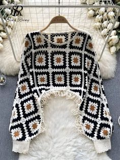 a black and white crocheted sweater hanging on a rack in front of a fur rug