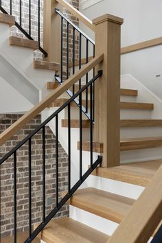 there is a wooden stair case next to the brick wall in this house with white stairs