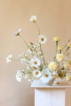 a vase filled with white and yellow flowers on top of a table next to a wall