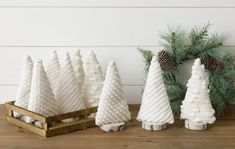 three white knitted christmas trees sitting on top of a wooden table next to pine cones