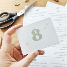 a person holding up a card with the number eight on it next to some scissors