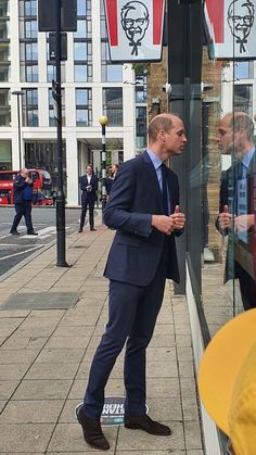 a man in a suit standing next to a window on the sidewalk with other people walking by