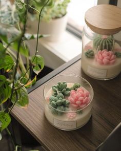 two glass jars with fake flowers in them on a table next to a potted plant