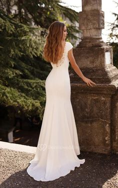 a woman in a wedding dress leaning against a stone pillar with her hand on the side