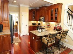 a kitchen with wooden cabinets and granite counter tops, along with hardwood flooring that matches the stairs leading up to the second floor