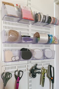 several bins with scissors and other items hanging on the side of a white wall