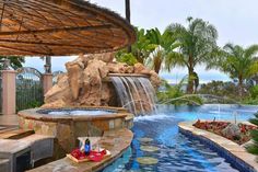 an outdoor swimming pool with waterfall and hot tub