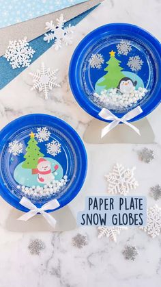 paper plate snow globes are displayed on a marble table with silver and blue decorations