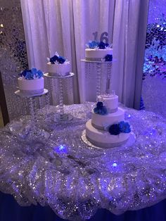 three tiered white wedding cake with blue flowers on the top and bottom, surrounded by sequins