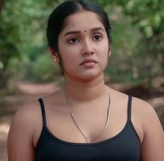 a woman in a black tank top is staring at the camera with trees in the background