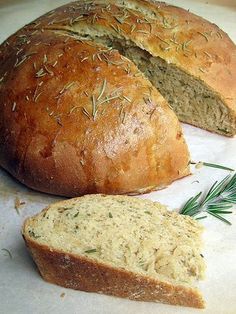 two loaves of bread with rosemary sprigs on top and one loaf cut in half