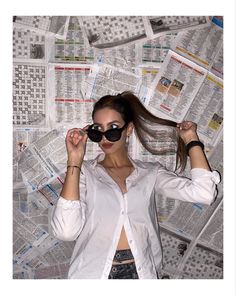 a woman wearing sunglasses standing in front of a wall covered with newspaper sheets and newspapers