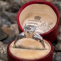 an engagement ring in a red velvet box on top of rocks with a diamond set in it