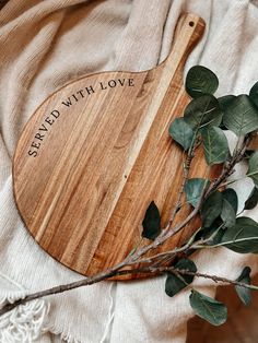 a wooden cutting board with the words spread with love on it and some green leaves