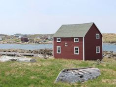 a red house sitting on top of a lush green field next to a body of water