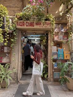 a woman is walking in front of a book store holding a bag and looking at her phone