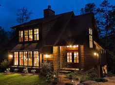 a large wooden house lit up at night with lights on the windows and shingled roof