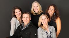 three women and two men are posing for a photo together in front of a black background