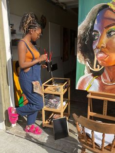 a woman standing in front of a painting on the side of a building next to a chair