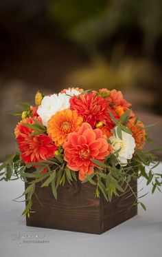 an orange and white flower arrangement in a wooden box with greenery on the side