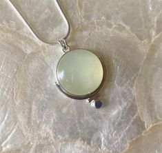 This pendant features a natural, round, Green Serpentine gemstone. This particular gemstone has natural, white, polkadot, inclusions that set it apart from the other gemstones. I knew I had to work with it 🥰 The semi-translucent nature and soft green color inspired me to make a simple but unique setting! I began by using a plain, silver, bezel wire, to secure the stone. Then, I attached a medium-size, plain, round, wire to frame part the stone, altering the silhouette of the stone just a bit. Then, I added a small piece of plain, round wire to fit against the other piece of plain wire. I did this to further alter the silhouette. Next, I added a flattened, sterling silver granule to the bottom of the piece. Lastly, I created a single, "V" bale (5mm), allowing for a variety of chains to be Round Jade Cabochon Necklace, Jade Cabochon Round Pendant Necklace, Round Jade Cabochon Pendant Necklace, Chalcedony Natural Stone Round Necklaces, Chalcedony Necklaces With Natural Stones, Jade Cabochon Round Pendant Jewelry, Spiritual Cabochon Necklaces, Elegant Gemstone Round Disc Necklace, Spiritual Cabochon Necklace