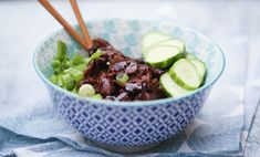 a bowl filled with meat and cucumbers on top of a blue table cloth