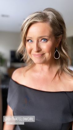 a woman in a black dress smiling at the camera with blue eyes and blonde hair