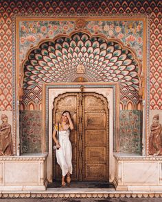 a woman standing in front of a wooden door with intricate carvings on the wall behind her