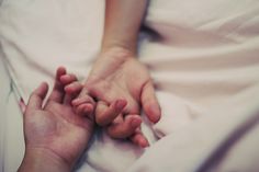 two hands holding each other while laying in bed