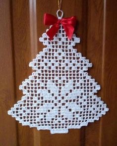 a crocheted christmas tree ornament hanging from a wooden door with a red bow