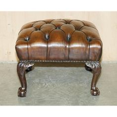 a brown leather ottoman sitting on top of a cement floor in front of a wall