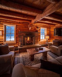 a living room filled with furniture and a fire place in the middle of a log cabin