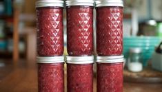 four jars filled with red liquid sitting on top of a wooden table next to each other