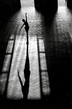 a person standing in the middle of a room with long shadows on the floor and windows