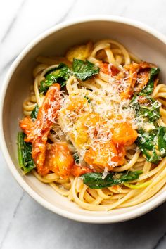 a white bowl filled with pasta and spinach on top of a marble countertop