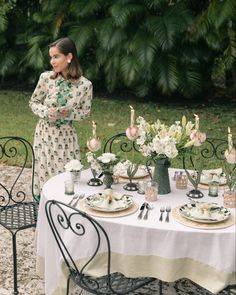 a woman standing next to a table with plates and flowers on it