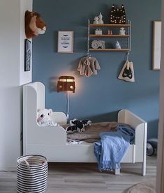 a bedroom with blue walls and white bedding, stuffed animals on the shelf above it