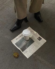 a newspaper with a coffee cup on the ground next to a person's legs