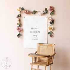 a happy birthday sign hanging on the wall next to a chair with flowers around it