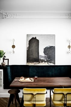 a dining room table with yellow chairs and a painting on the wall