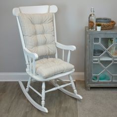 a white rocking chair next to a gray side table with a bottle and glass on it