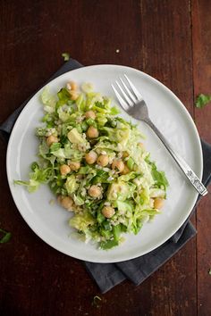 a white plate topped with lettuce and chickpeas next to a fork