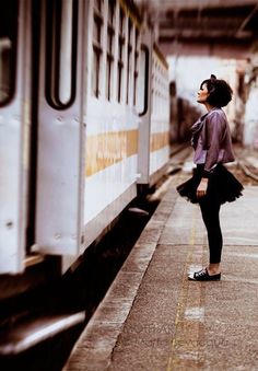 a woman standing next to a train on the tracks