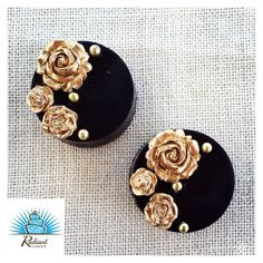 two black and gold earrings with flowers on top of each earring, sitting on a piece of fabric