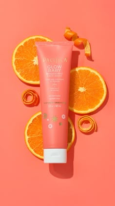 an orange slice next to a tube of glow baby sunscreen on a pink background