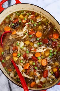 a red pot filled with meat and vegetables on top of a marble countertop next to a spoon