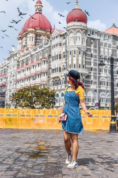 a woman walking in front of a large building with birds flying around her and on the ground